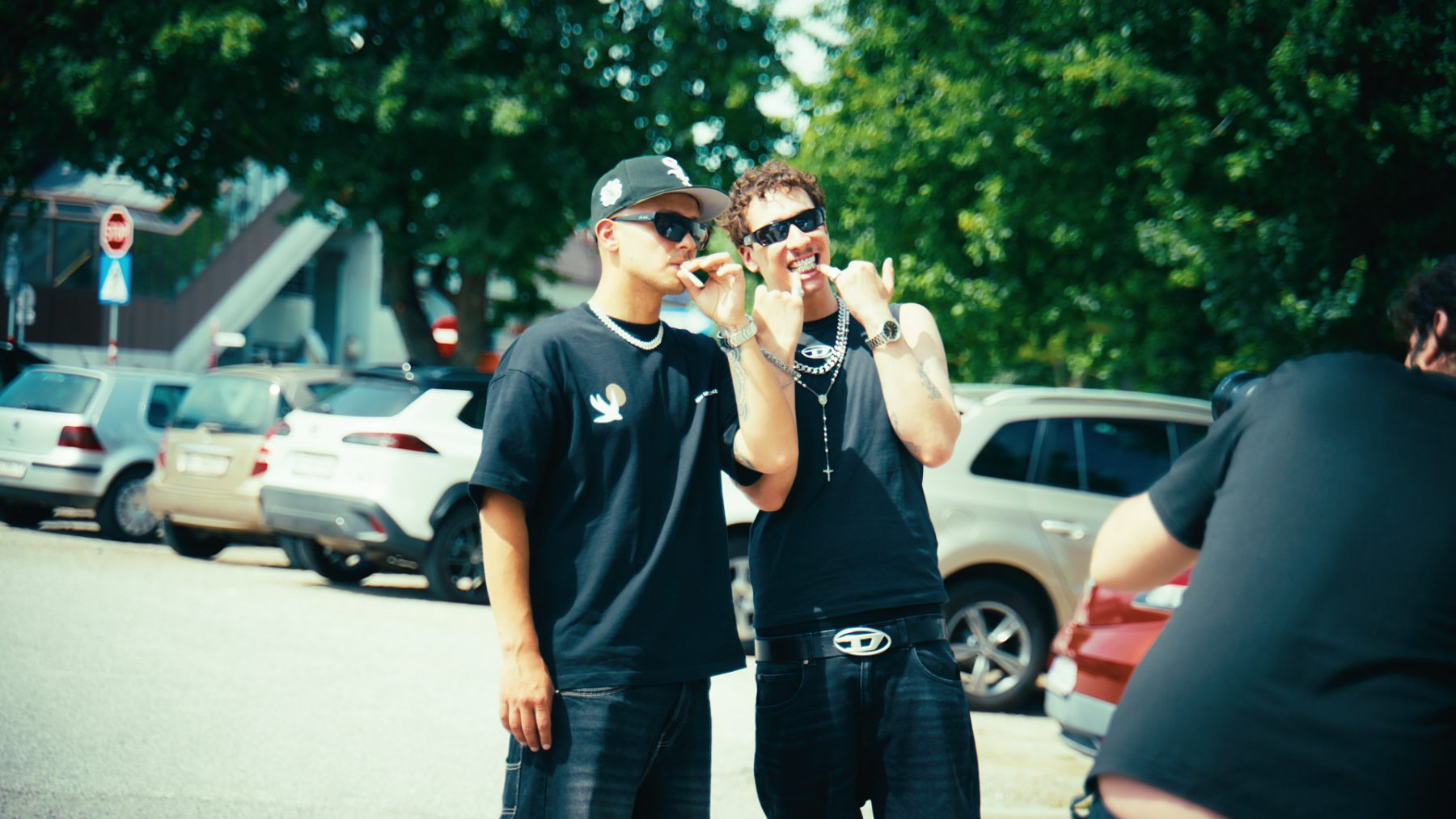 The two artists in sunglasses and chains on the parking-lot set