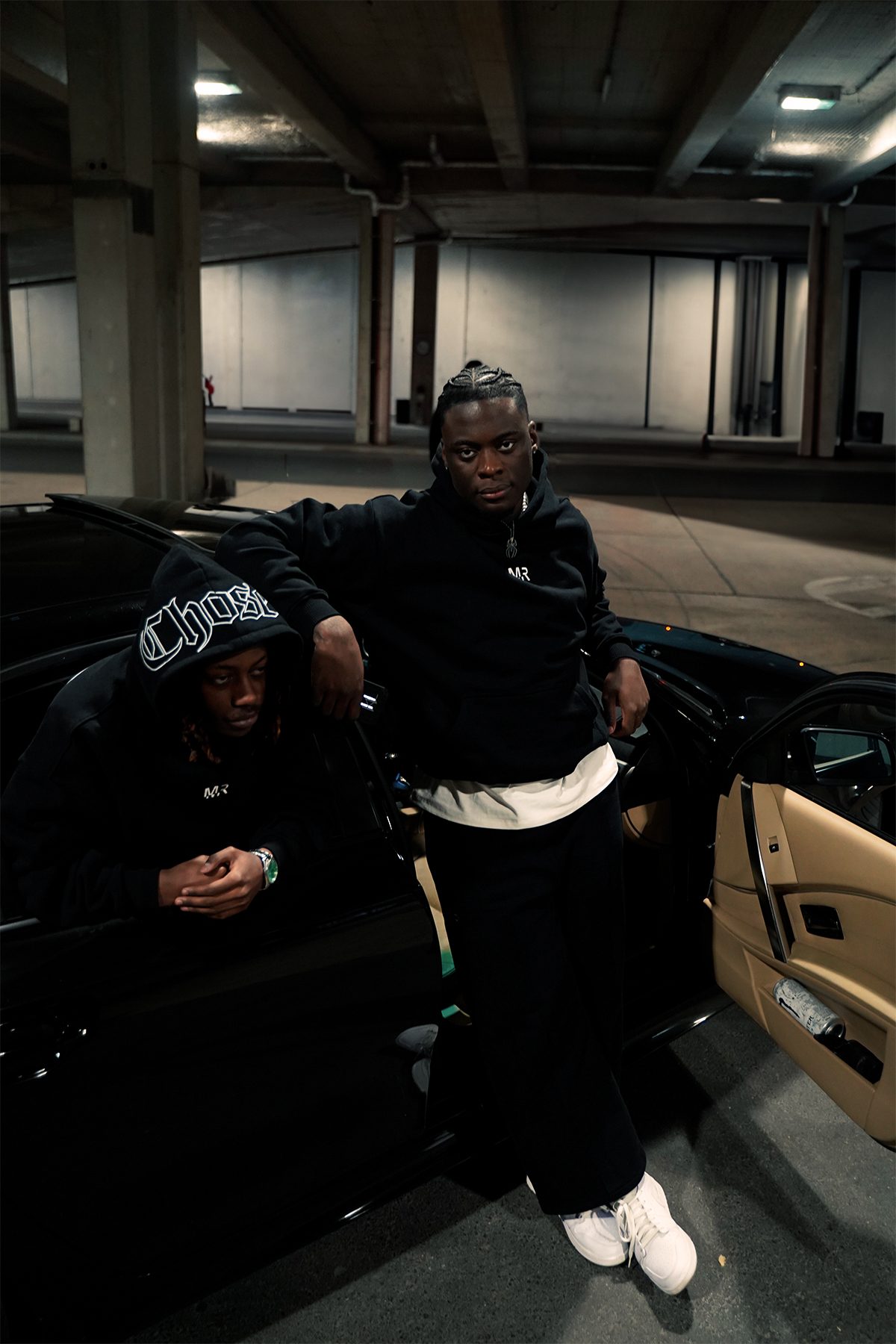 Two models in Money Revenge hoodies leaning on an open car door