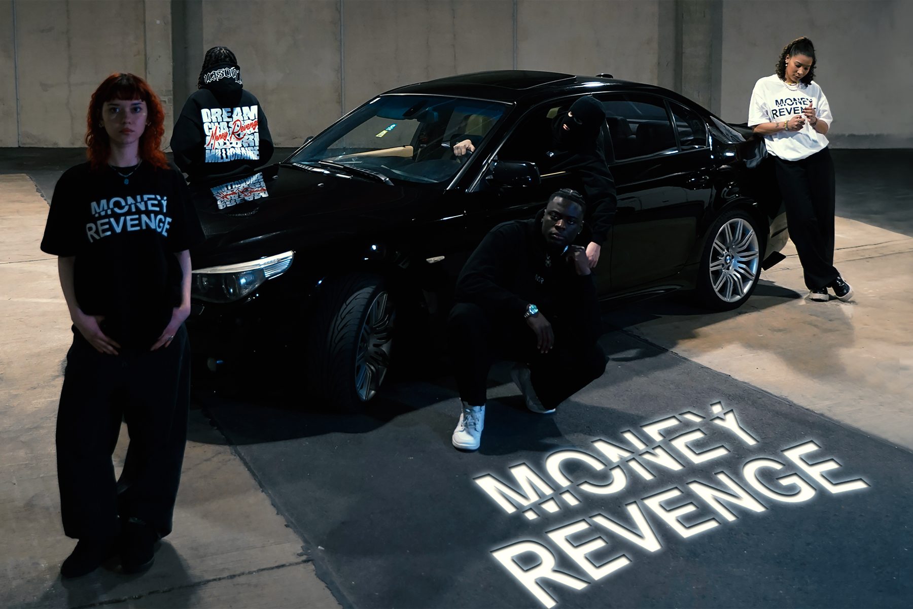 The crew around a black BMW in a garage, the Money Revenge logo projected across the floor