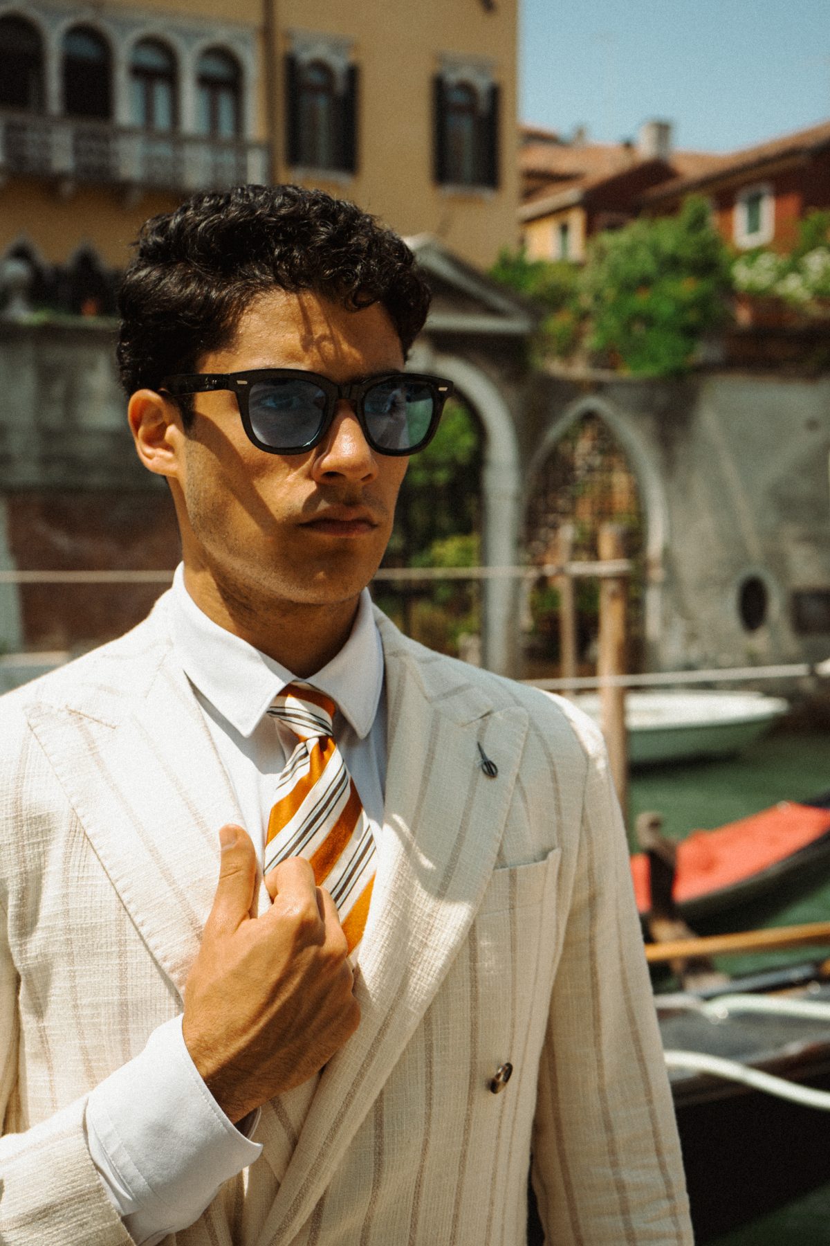 Model in a cream pinstripe suit adjusting his tie by a canal