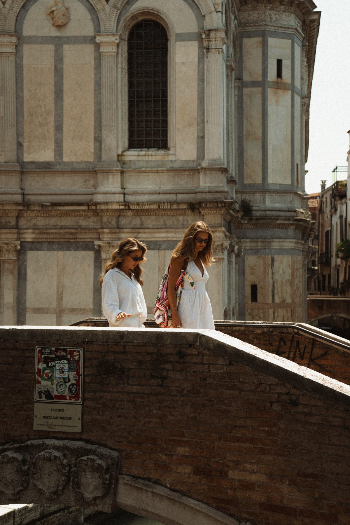 Two women in white crossing a bridge in front of a marble church facade